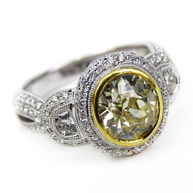 Approx. 1.80 Carat Oval Cushion Cut Fancy Yellow Diamond and 18 Karat White Gold Engagement Ring Accented throughout with Approx. 1.42 Carat Trapezoid and Round Brilliant Cut Diamonds.