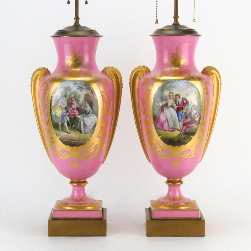 Pair of Antique Sevres Style Porcelain Urn Lamps. Gilt hand painted scrolling on rose ground with mock figural handles, courting scene and flower study windows. 